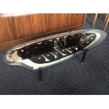 A mid 20th Century black and mirrored topped shaped glass coffee table with leaf decoration.