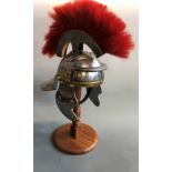 A replica Roman Centurions helmet with red brush top and cheek guards on wood stand