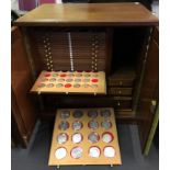 A mahogany coin display cabinet with 30 sliding drawers containing a large selection of coins to
