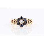 A diamond and sapphire flower cluster ring, set with a central round brilliant cut diamond
