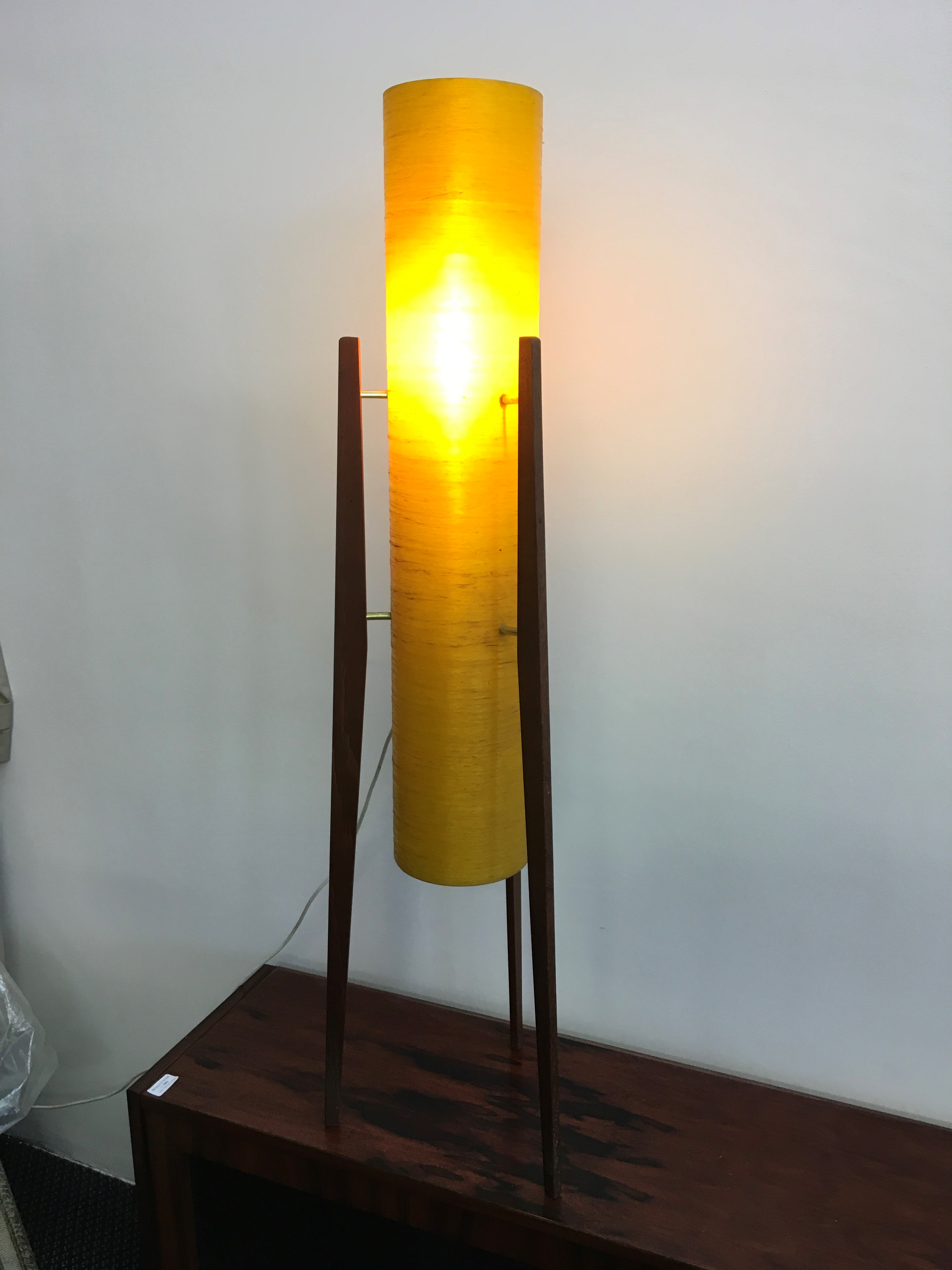 An orange cylinder mid century floor standing light fitting standing on three legs.