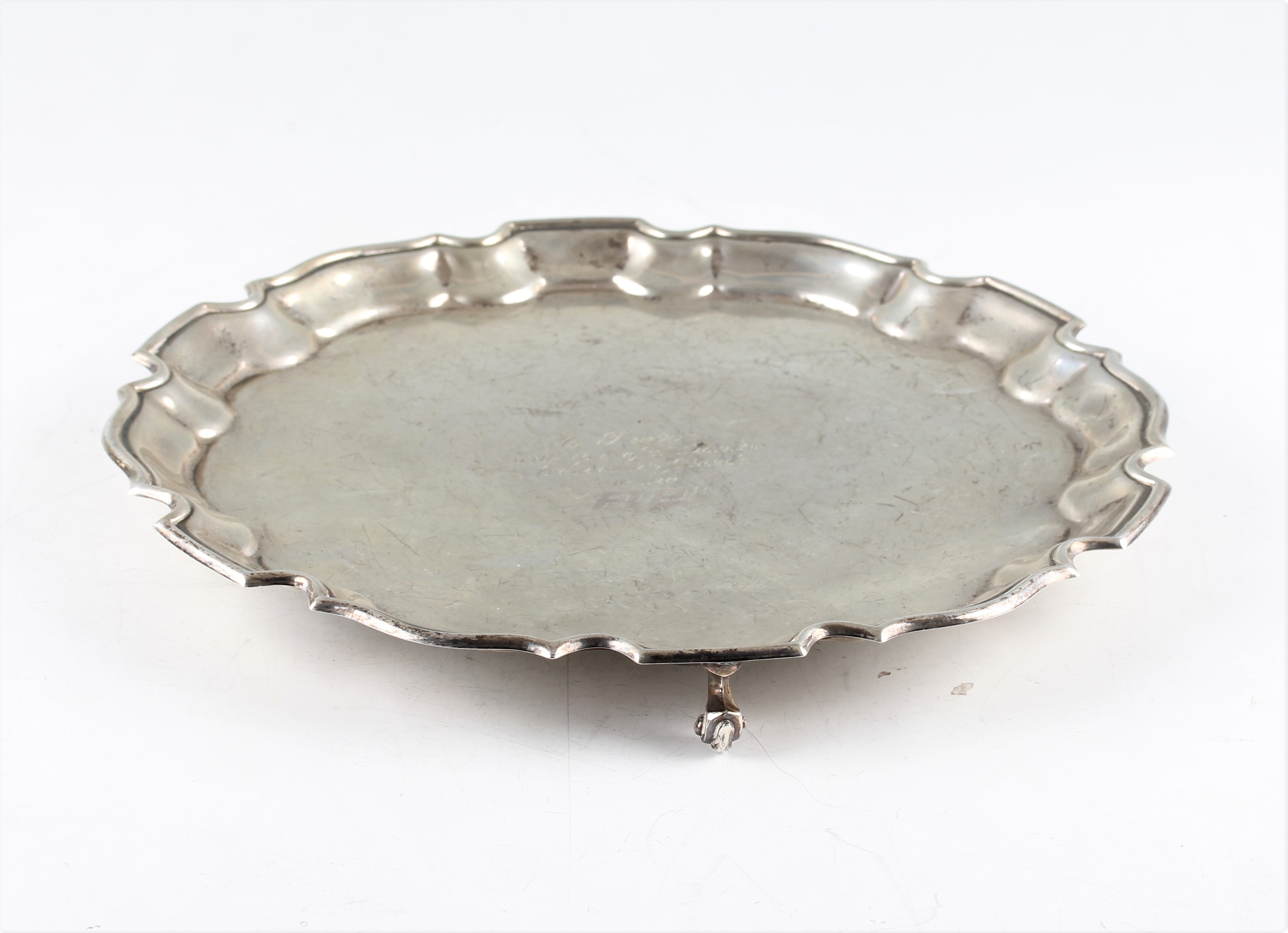 A silver salver, the circular form with pie crust rim and central personal engraving, raised on