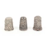 Three silver thimbles comprising an unusual example decorated with cherubs capturing another and