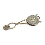 A silvered brass skirt lifter, of scissor form the circular sliding boss decorated in relief to each