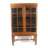 A 1930's oak two door cabinet in the Arts and Crafts Style enclosed by a pair of bar glazed doors,