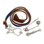 Three skirt lifters, comprising a white metal 'Bijou' on blue and brown cord suspension with tassel,