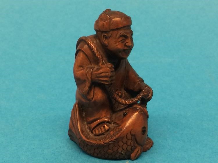 A carved wooden Netsuke in the form of a man catching a fish