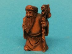 A carved wooden Netsuke in the form of a man holding a staff