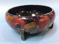 A William Moorcroft pottery bowl, decorated with pomegranates, on a dark blue ground, in the Arts