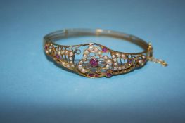 A yellow metal bangle, decorated with garnets and seed pearls, 12.1g