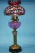 A Victorian oil lamp with cranberry coloured and floral painted shade, cranberry reservoir and