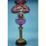 A Victorian oil lamp with cranberry coloured and floral painted shade, cranberry reservoir and