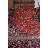 A large Kashan carpet, red ground with a central blue floral medallion, large main flower head