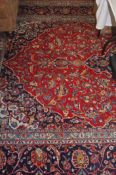 A large Kashan carpet, red ground with a central blue floral medallion, large main flower head