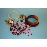 An amber coloured bangle, two other bangles, two necklaces, a lion brooch and a bracelet.