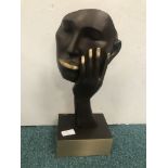 An abstract bronze sculpture of a woman with hand on cheek