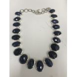 A Silver and Sapphire Necklace: 19 graduated oval harlequin facet cut sapphires set in silver with