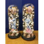 A pair of glass domes containing ceramic fishers and floral surrounds