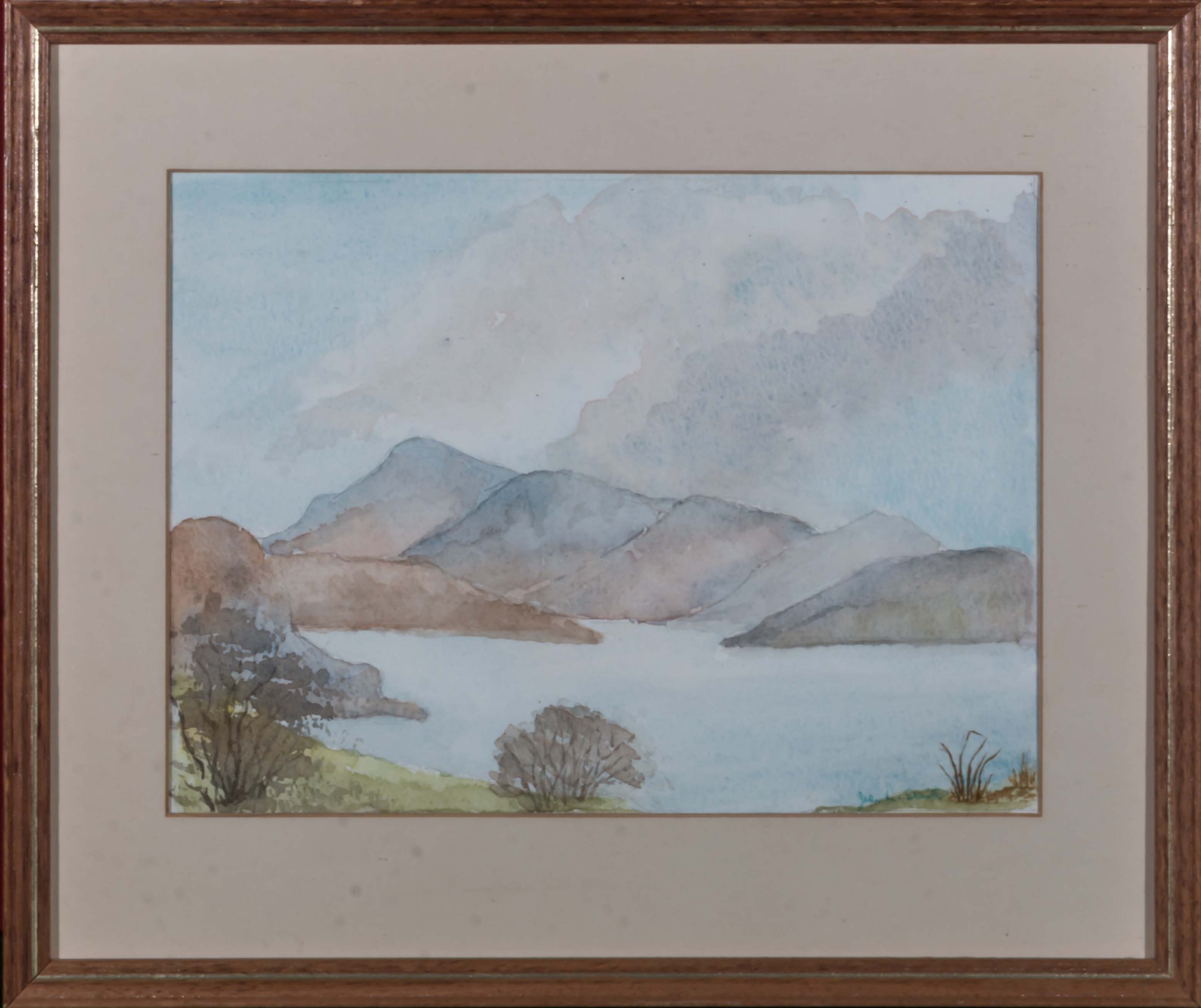 A small framed watercolour depicting a lake and mountain scene, indistinct signature