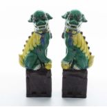 A pair of Chinese green and yellow glazed temple dogs on brown glazed bases