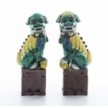 A pair of Chinese green and yellow glazed temple dogs on brown glazed bases