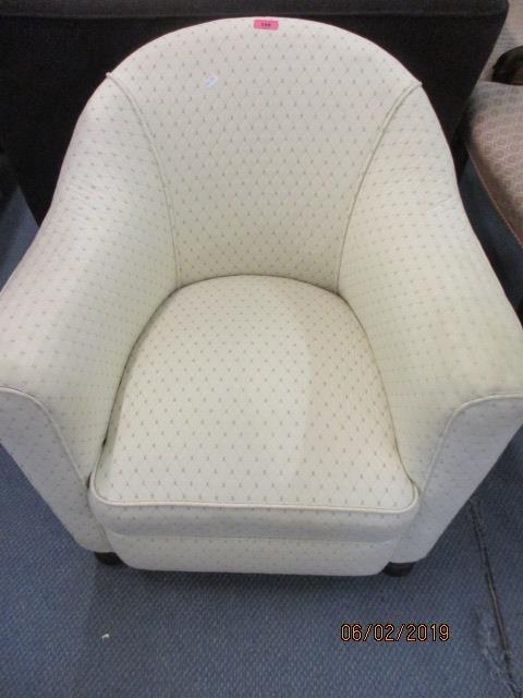 A low cream upholstered tub chair with front bulbous feet