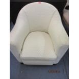 A low cream upholstered tub chair with front bulbous feet
