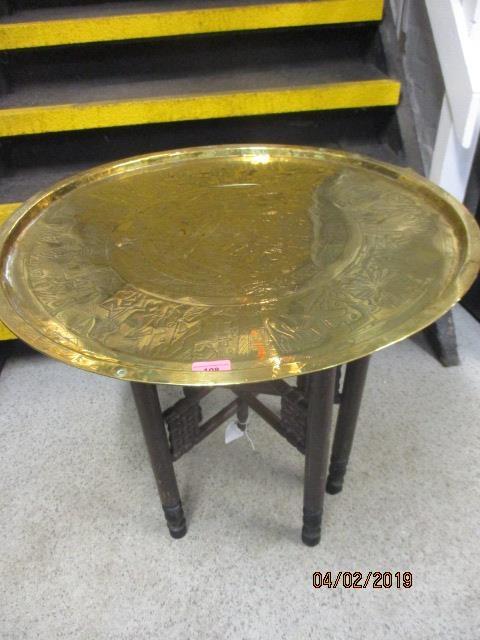 An brass tray topped table on a folding wooden stand, the tray depicting Egyptian scenes