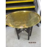 An brass tray topped table on a folding wooden stand, the tray depicting Egyptian scenes
