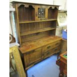 An Arts & Crafts oak dresser having a plate rack above a single cupboard and two drawers