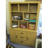 A modern light wood display cabinet with open shelves to the top and drawers and cupboards, below,