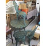 A green painted wrought iron two tier garden table with umbrella stand and three chairs