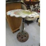 A cast and stamped metal bird bath, the top of shell form with bird perched on the edge, supported