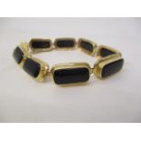 A gold coloured eight link bracelet set with eight black cabochons, in stepped, pierced frames,