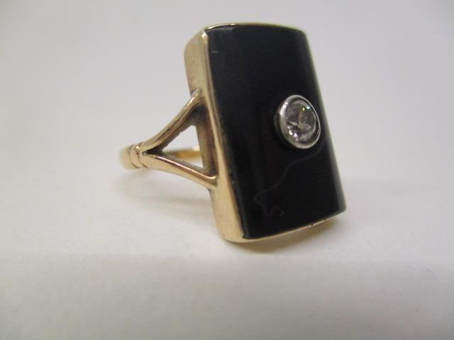 A gold coloured ring set with a central diamond on a black curved tablet and panelled back, size