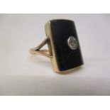 A gold coloured ring set with a central diamond on a black curved tablet and panelled back, size