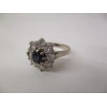 A white gold coloured metal ring set with a central sapphire, surrounded by eight diamonds,