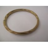 A gold coloured metal bangle with rope twist style ornament, stamped 9kt, 11.7g total