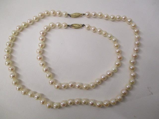 A pearl necklace and matching bracelet, each with a gold coloured metal pierced clasp, stamped 14k