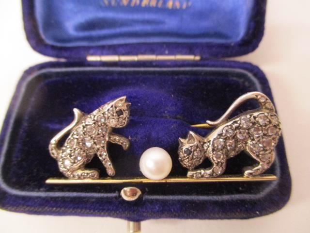 A gold and white coloured metal brooch fashioned as two kittens playing with a pearl, set with