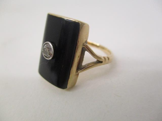 A gold coloured ring set with a central diamond on a black curved tablet and panelled back, size - Image 2 of 3