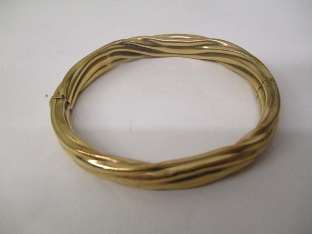 A gold coloured metal bangle with rope twist style ornament, stamped 9kt, 22.2g total