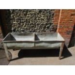 A galvanized steel double cattle trough on angular legs 32"h x 74"w