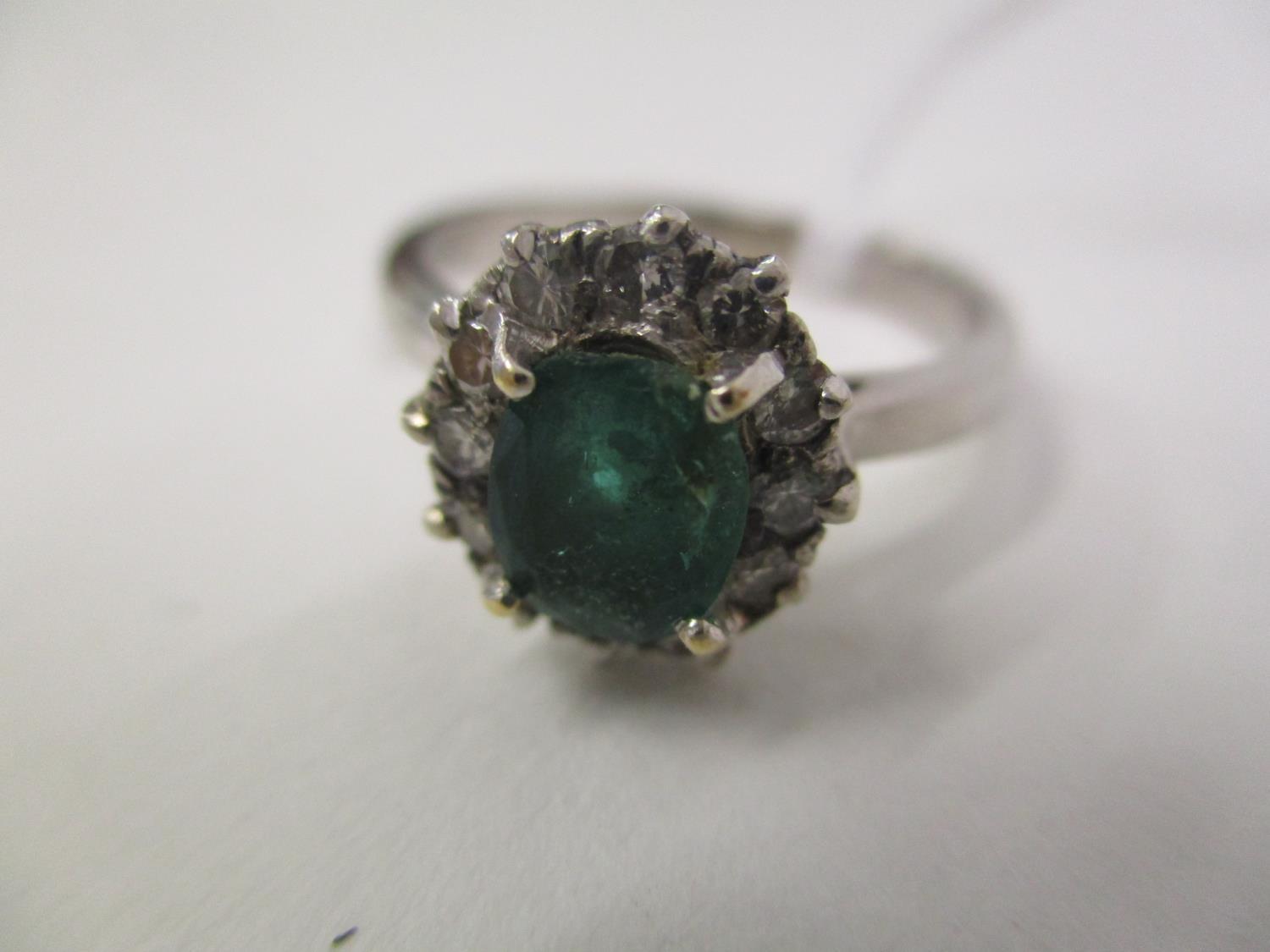 A white gold coloured ring set with an emerald within a band of diamonds, 4g