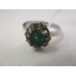 A white gold coloured ring set with an emerald within a band of diamonds, 4g