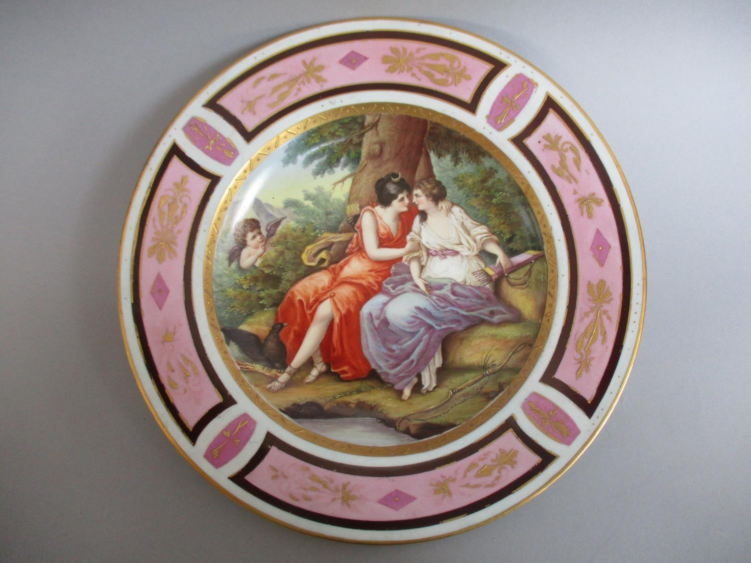 A late 19th century plate painted with two women embracing under a tree with bows and arrows by them