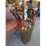 A modern basket style umbrella stand containing modern umbrellas, walking sticks,