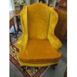 A George III wing backed armchair in a mustard yellow velour upholstery with carved front cabriole