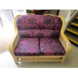 A wicker two-seater couch with upholstered loose cushions in a floral two-tone purple fabric