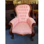 A carved oak button back armchair upholstered in a floral pink fabric on French knee carved and